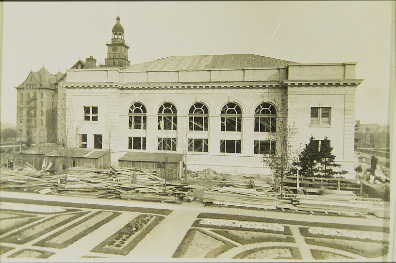 Black and white photo of Schwab Auditorium under construction. Old Main in background. Flower gardens in foreground.